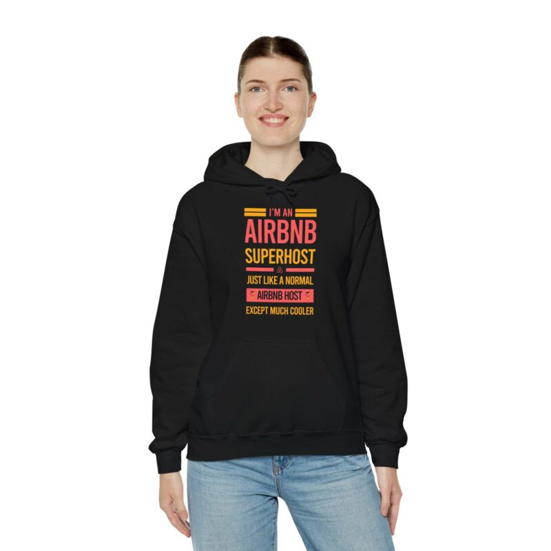 Individual donning an "I'm an Airbnb Superhost Unisex Heavy Blend Hooded Sweatshirt" in black, featuring a vibrant printed message declaring, "I'm an Airbnb Superhost, just like a normal Airbnb host except much cooler.