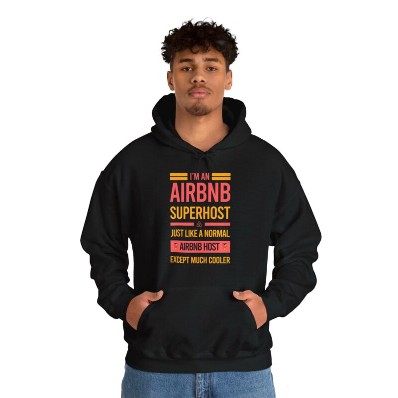 A person wearing an "I'm an Airbnb Superhost Unisex Heavy Blend Hooded Sweatshirt," featuring the text: "I'm an AirBnB Superhost, just like a normal AirBnB host except much cooler," stands against a plain white background.