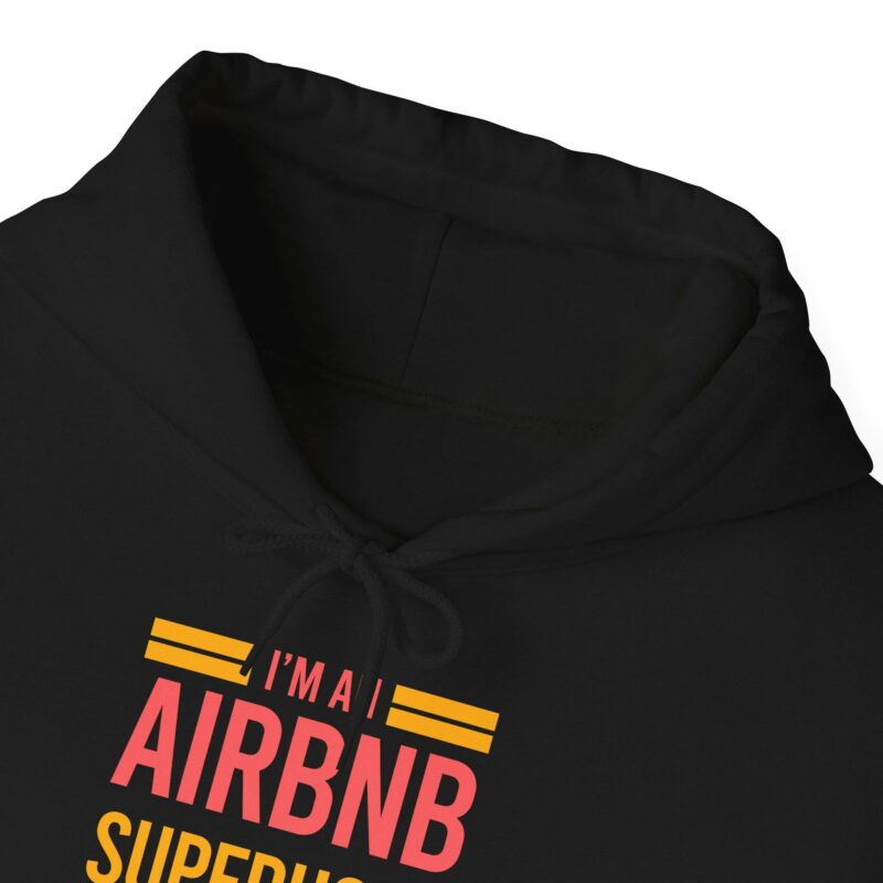 A close-up of the "I'm an Airbnb Superhost Unisex Heavy Blend Hooded Sweatshirt" in black, featuring the text "I'm an Airbnb Superhost" printed in red and yellow on the front.