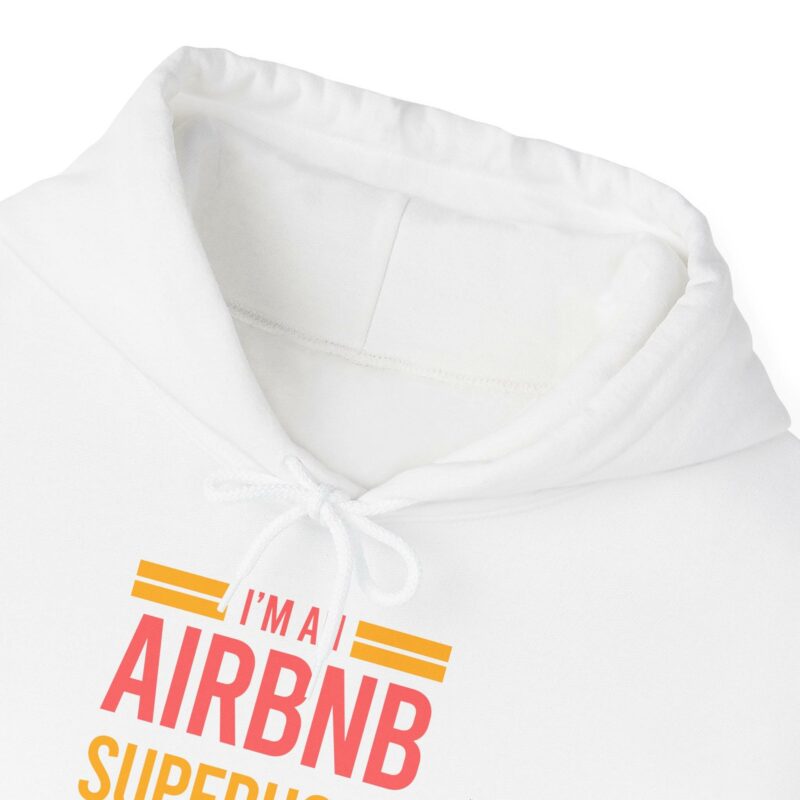 A close-up of the hood and front text of a white "I'm an Airbnb Superhost Unisex Heavy Blend Hooded Sweatshirt" that reads "I'M A AIRBNB SUPERHOS." The text is in red and pink with yellow lines above and below the main words.