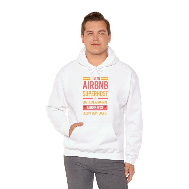 A man wearing the "I'm an Airbnb Superhost Unisex Heavy Blend Hooded Sweatshirt," featuring text that says, "I'm an Airbnb Superhost, just like a normal Airbnb host except much cooler," stands with one hand in his pocket.