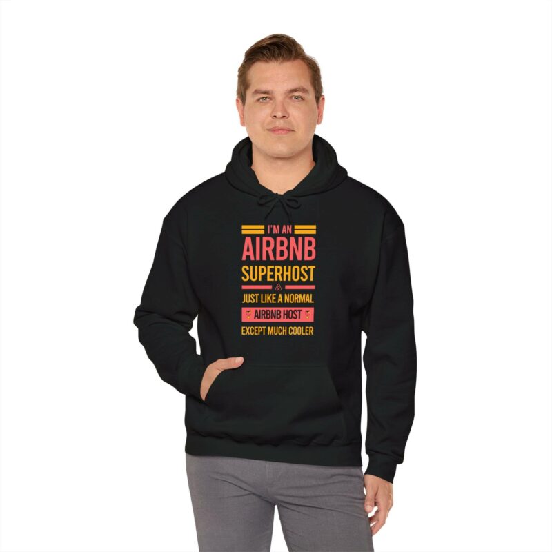 The person is wearing the "I'm an Airbnb Superhost Unisex Heavy Blend Hooded Sweatshirt" in black, featuring a text design that reads, "I'M AN AIRBNB SUPERHOST - JUST LIKE A NORMAL AIRBNB HOST, EXCEPT MUCH COOLER.