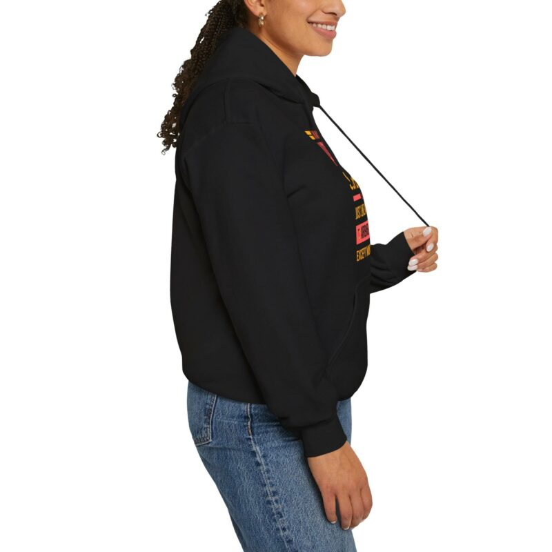 A person wearing the "I'm an Airbnb Superhost" unisex heavy blend hooded sweatshirt with colorful graphics is pulling the drawstring. They are also wearing blue jeans with visible stitching.