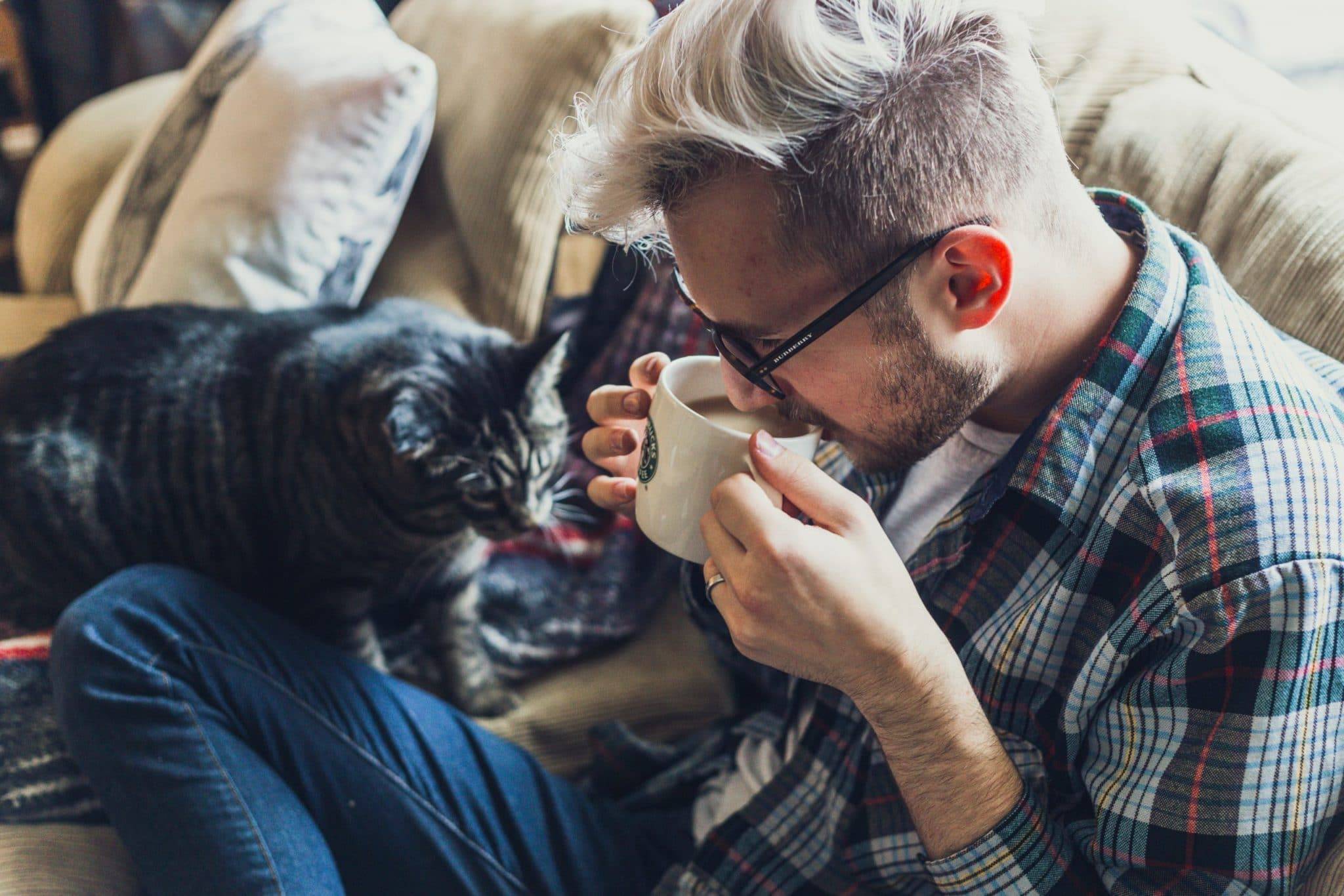 Airbnb Hosting A man relaxing with coffee and a cat on an Airbnb couch.