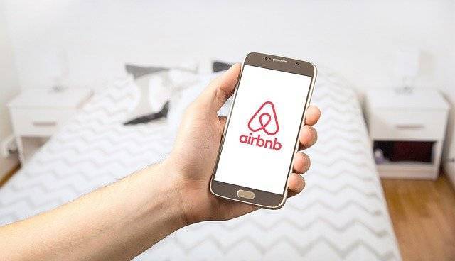Airbnb Hosting A person holding up a cell phone with the Airbnb logo on it, sharing Airbnb tips.
