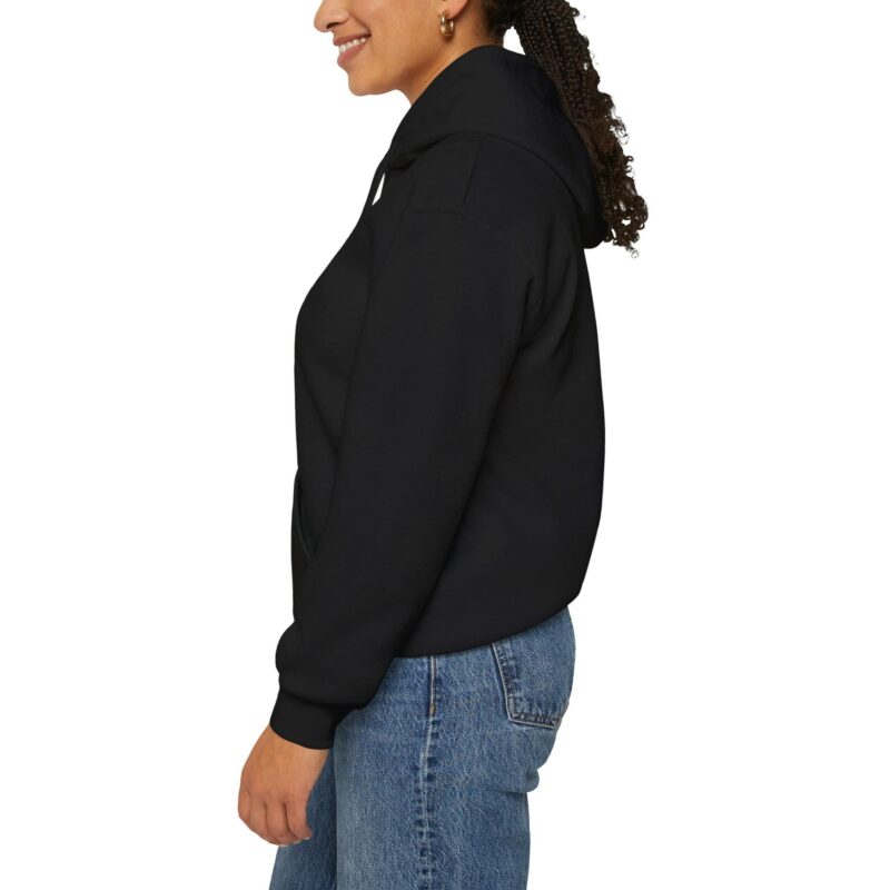 Person wearing an "I'm an Airbnb Superhost" unisex heavy blend hooded sweatshirt and blue jeans, standing sideways and smiling.