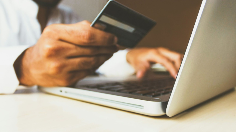 A person in a white shirt holds a credit card while using a laptop on a light-colored desk, embodying the essence of 5 simple tips to start an eCommerce business and lead it to success.