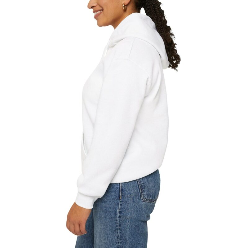 Person wearing an "I'm an Airbnb Superhost" Unisex Heavy Blend Hooded Sweatshirt and blue jeans smiles while standing sideways against a plain white background.