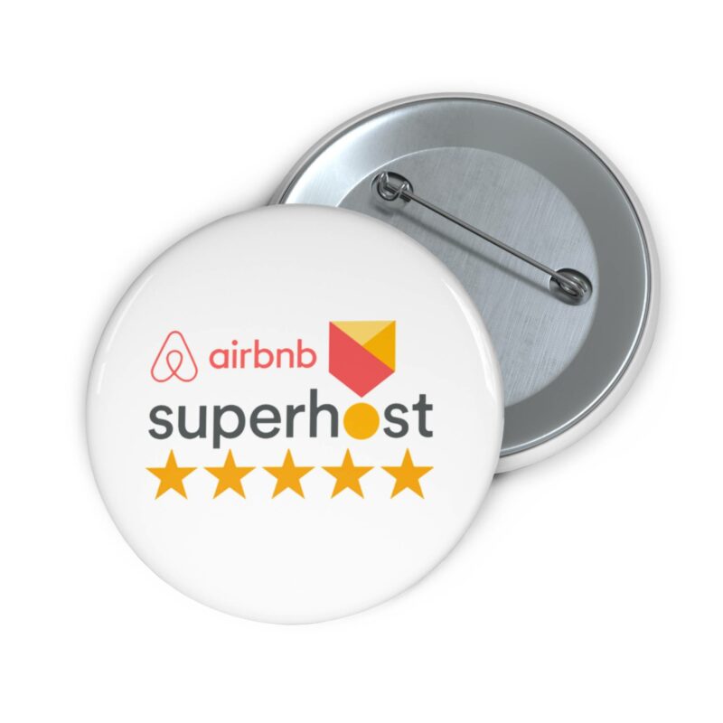 The Airbnb Superhost Pin Buttons feature the Superhost logo with five stars, making them an ideal accessory for those beginning their Airbnb hosting adventure or looking to elevate their hosting experience; they are displayed partially open against a white background.