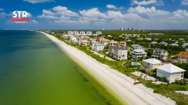 Airbnb Hosting An aerial view of a beach with green water and houses, showcasing a serene guest experience for Airbnb management.