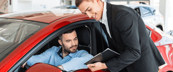 Airbnb Hosting A man in a business suit is talking to a man in a car showroom, discussing how to elevate his Airbnb hosting game with 17 tips.