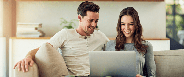 Airbnb Hosting A man and woman are sitting on a couch and using a laptop to Elevate Your Airbnb Hosting Game with 17 Tips.